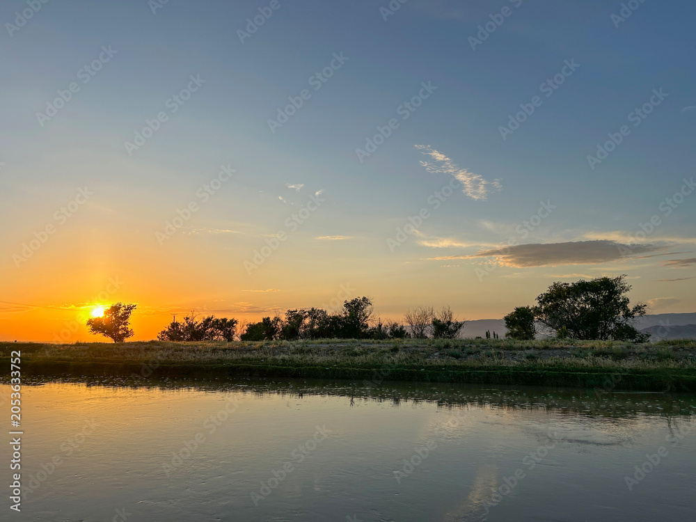 Obraz premium Beautiful golden sunset over a calm river and tree-lined bank