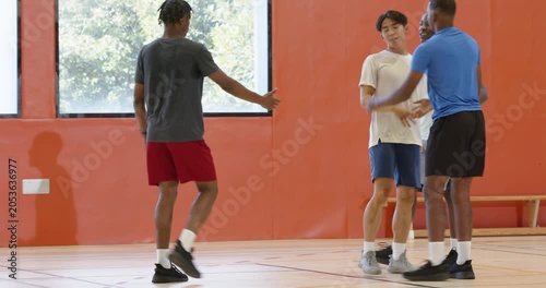 Dribbling basketball causing defender fall diverse male teammates, lifting up and resetting play
