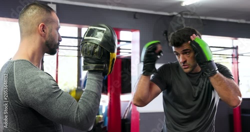 Trainer and indian trainee responding to mitt signals, throwing jabs and weaving under pads in gym