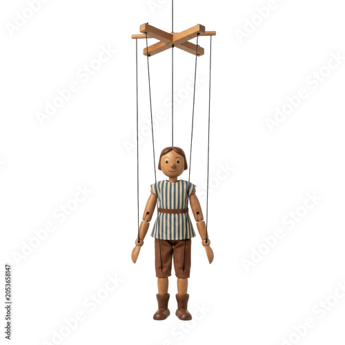 A wooden marionette puppet with articulated limbs and a control cross, standing on a transparent background. The puppet is dressed in a striped shirt and shorts.