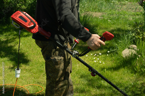 Photos Man is mowing the grass with an electric trimmer in the summer garden