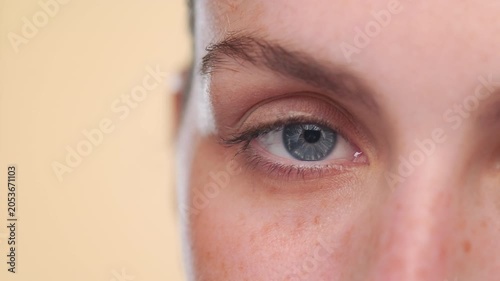 Detail shot of young light-complexioned Latina opening her eye on beige background | skin care commercial concept