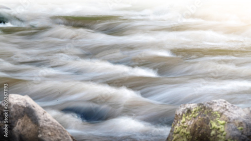 Принти на полотні Long exposure shot of fast-flowing river water rushing between rocks, creating a