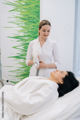 Foto Vertical portrait of female beautician using rf lifting device on mature woman client face for non surgical facelift, stimulating collagen production for smoother, firmer, more youthful looking skin