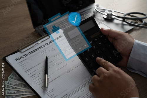 Fotografía Hands using a calculator above a health insurance claim form with cash, laptop,