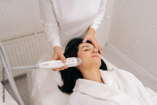 Top view of relaxed adult woman receiving innovative rf microneedling facelift procedure from skilled esthetician, modern hardware cosmetology method for skin tightening and wrinkle reduction.