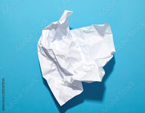 A crumpled white paper ball rests on a bright blue surface, casting a soft shadow