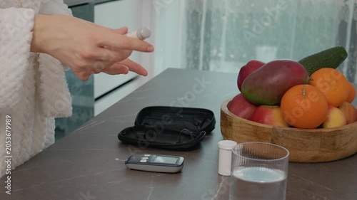 A woman performs a blood glucose test in her kitchen. She prepares to check her blood sugar level next to a bowl of fresh fruits after measuring her levels.
