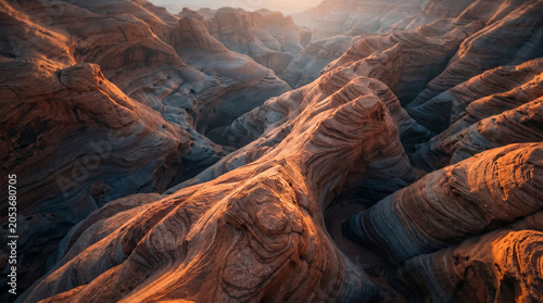 Sweeping aerial view of eroded sandstone canyons with dramatic light and shadow highlighting stratified layers and natural formations in a desert environment.