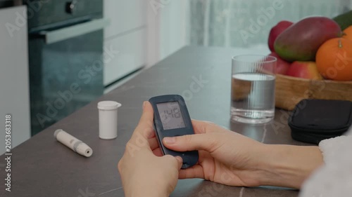 In a kitchen, a woman looks at the glucometer diary, swiping through past blood sugar results. She monitors her health by reviewing the glucose history carefully.