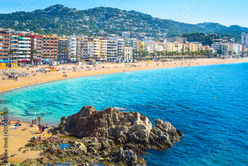 Fotografía Beautiful coastal view of a sandy bay and turquoise sea with prominent rocks in Lloret de Mar on a sunny day, Costa Brava, Catalonia, Spain