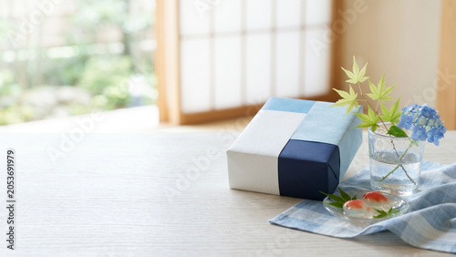和室の卓上に置かれた夏の贈答品と涼やかな紫陽花、青もみじとガラスの器に添えた和菓子をやわらかな自然光で捉えた、上品で季節感あふれる日本の夏イメージ。お中元、暑中見舞い、夏の挨拶、和のしつらえ、暮らし、販促や広告デザインに使いやすいコピースペース付きの和風静物素材