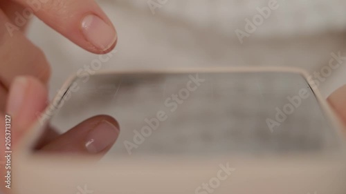 A person is using a smartphone with both hands while interacting with others in a home setting. Focus is on the hands and device during the activity.