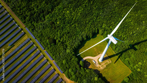 Aerial top down view of solar panels next to a wind turbine and forest with renewable energy