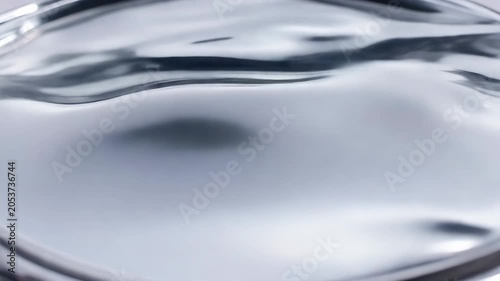 Smooth monochrome silver liquid metal surface rippling gently with metallic reflection and fluid waves. Futuristic chrome material design concept