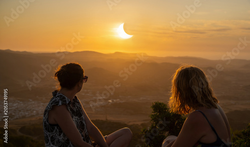 Tableau sur toile Two women friends in summer dresses looking at a spectacular partial solar eclip