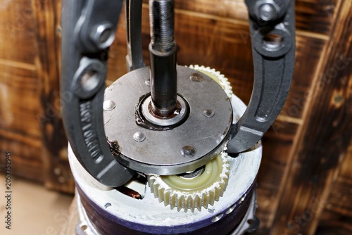 Three-jaw gear puller removing an overrunning clutch from a geared electric motor hub, performing DIY maintenance and repair of an e-bike motor assembly in a home workshop