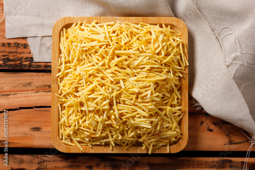 Fotografie Crispy yellow shoestring potatoes stacked on a square wooden serving platter wit