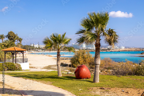 Canvastavla Cozy resort park zone with palm trees, clay jar and wooden gazebo on green grass lawn near sandy beach bay