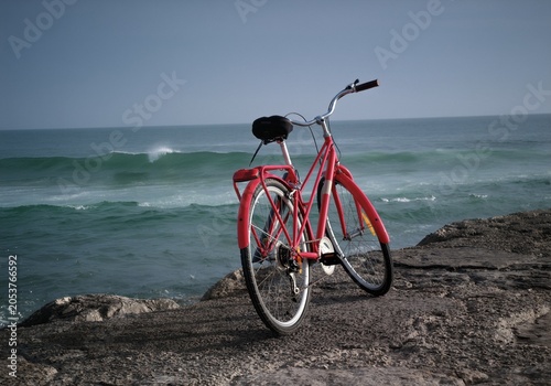 Bright red vintage bicycle parked on a rocky stone ledge overlooking the calm blue ocean waves