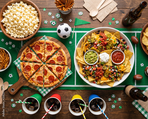 Top view football game day snack spread with pizza nachos popcorn and drinks for party table background