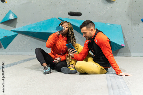 Woman drinking water and man looking at phone at the gym