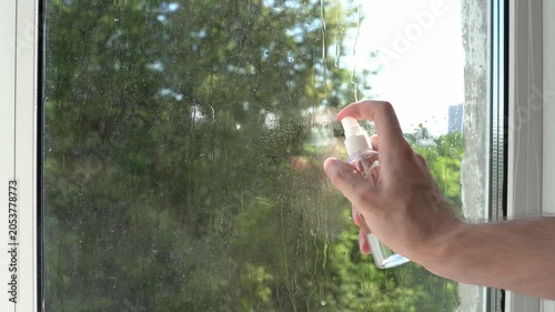 Young man's hand spraying water on glass from window cleaning sprayer in summer as a general cleaning concept of house
