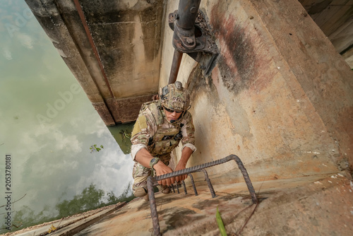 Soldier climbs a wall during military training near a waterway in bright daylight