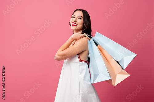 Obraz na plátně Stylish young woman in trendy outfit holding shopping bags against pink backgrou