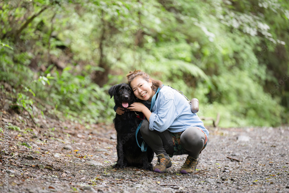 Fototapeta premium 森の中で愛犬と触れ合いながら笑顔を見せる女性のアウトドアライフカメラ目線
