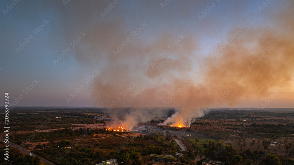 Fototapeta premium Aerial view of Smoke from burning fields spreads across the rural sky, slowly erasing the colors of sunset and turning a peaceful evening into a sign of environmental harm.