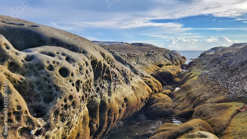 Schilderij op canvas Panoramic landscape of massive coastal rock formations with distinct honeycomb patterns lining a narrow channel leading toward the sea
