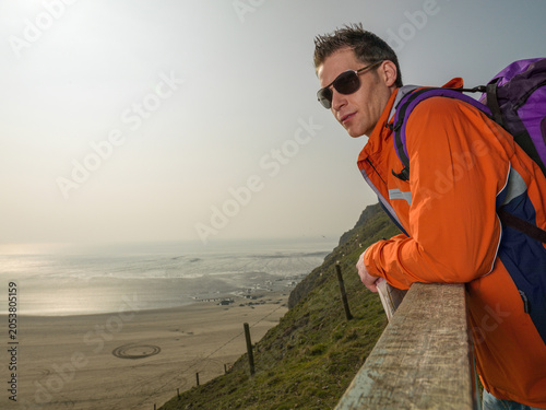 Foto Young male hiker looking back to camera with coastal landscape behind
