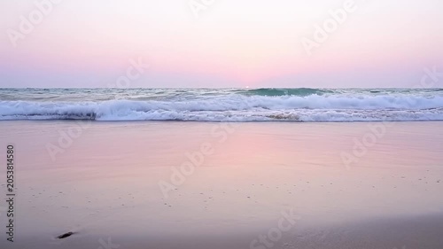 Ocean waves crashing on sandy shoreline at sunset or sunrise