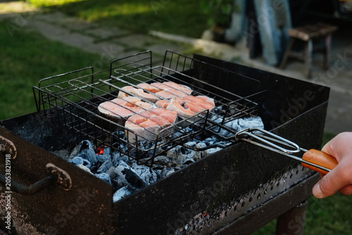 Man grilling steaks of salmon fish in backyard. Summer weekend activity, barbecue, cookout.