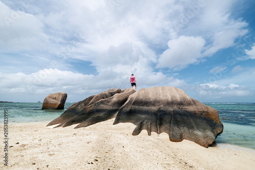 Tablou pe pânză Tourist standing on top of granite rock in Seychelles and looking around at horizon