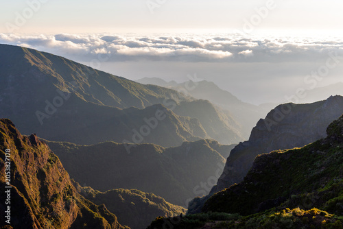 Pico do Arieiro sunrise over Madeira's rugged peaks. Dramatic mountain ridges, clouds drifting through valleys. Hiking trails wind through volcanic terrain. Portugal's island landscape at dawn.