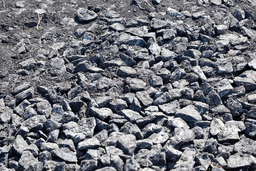 Close-up view of rough black gravel stones scattered on the ground, showcasing various sizes and textures in a natural outdoor setting