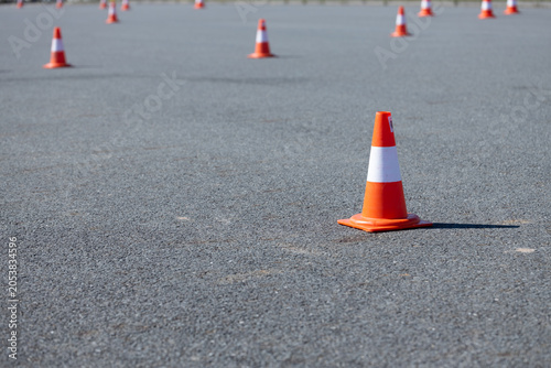 Orange traffic cones arranged on a paved surface in an outdoor setting, with a clear blue sky and distant horizon visible in the background
