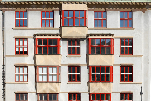 Architectural facade of a building featuring multiple windows with red frames and a beige exterior, showcasing a modern design in an urban setting