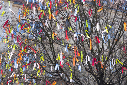 Easter. Colorful ribbons of various hues tied to bare branches of a tree, creating a vibrant display against a blurred building backdrop