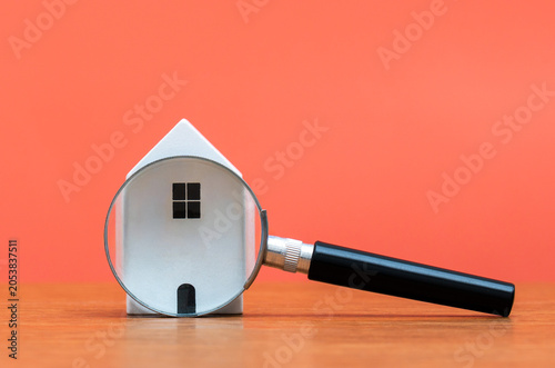 A miniature white house viewed through a magnifying glass. Real estate search, property inspection, housing market analysis, and mortgage appraisal concepts.