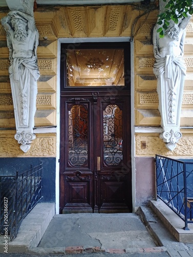 Fotografie Historic entrance portal of a European building featuring an elegant carved wooden double door with ornate iron grilles, flanked by classic white stucco atlantes sculptures