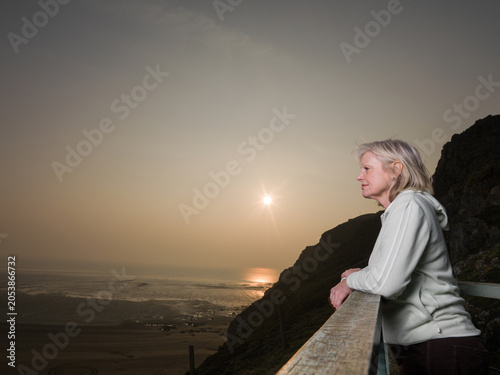 Photos Senior female leaning on barrier looking over sea and beach at sunset