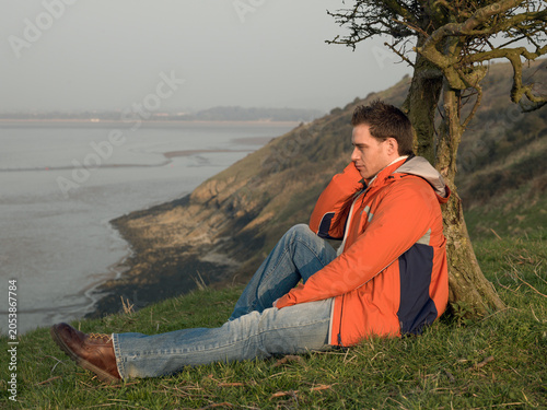 Fotografie Young man in orange hiking jacket looking at view over coastline