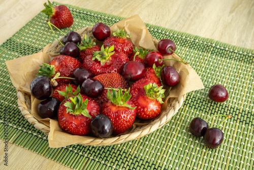 Fresh ripe red strawberries and sweet cherry in a woven basket on green placemat