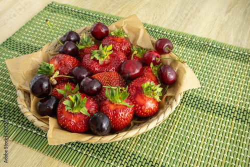 Fresh ripe red strawberries and sweet cherry in a woven basket on green placemat