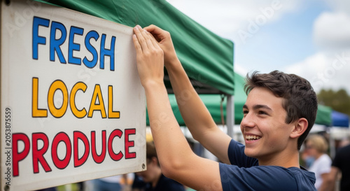 Smiling Young Man Hanging 'Fresh Local Produce' Sign at Outdoor Market