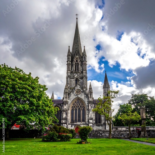 A large gray church with a tall spire and arched windows under a cloudy blue sky