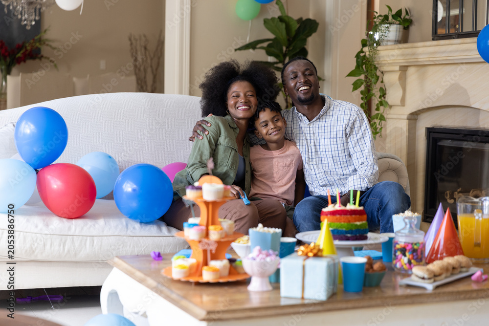 Obraz premium Parents and son sitting on white couch in living room with rainbow cake and balloons